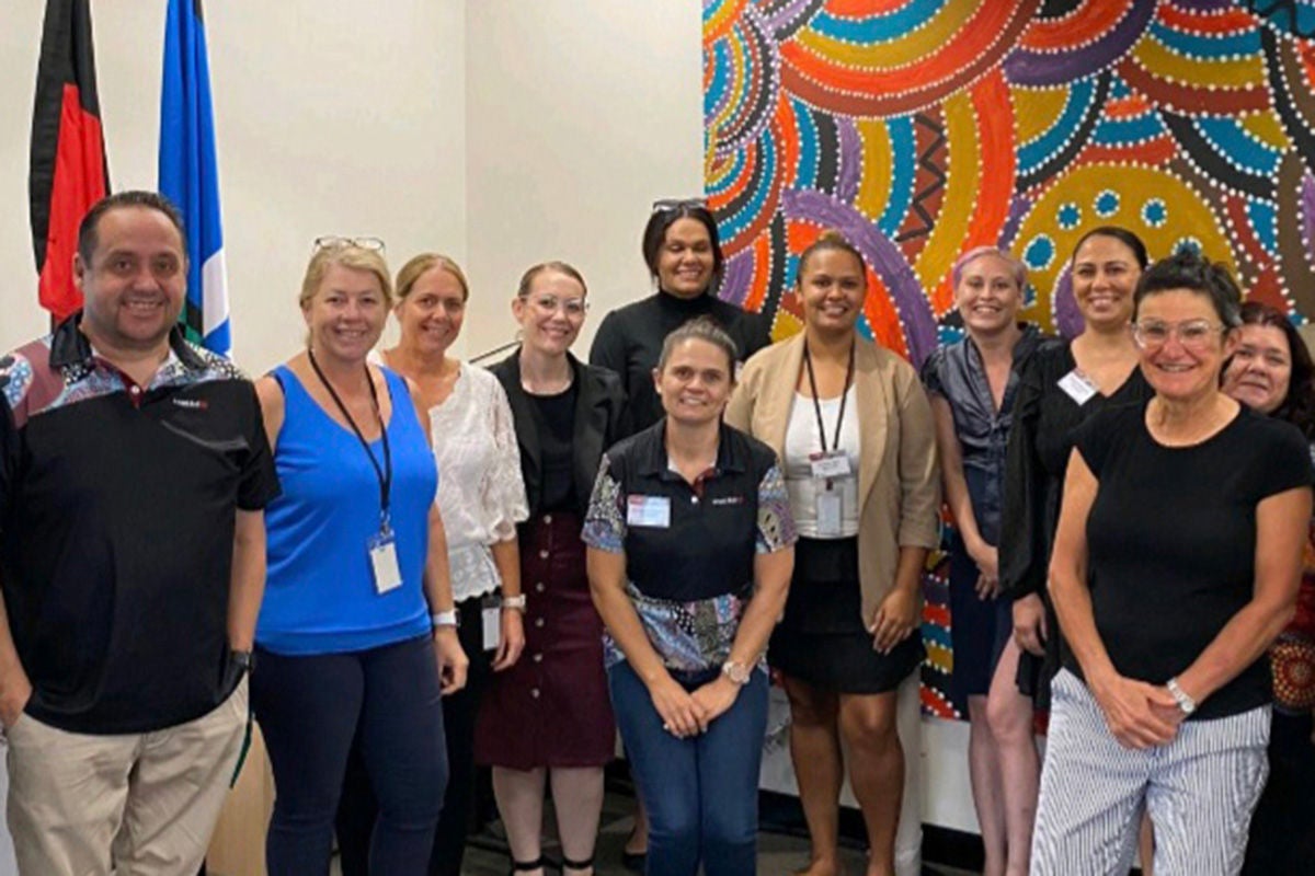 Group of professional people smiling in front of colourful Aboriginal artwork