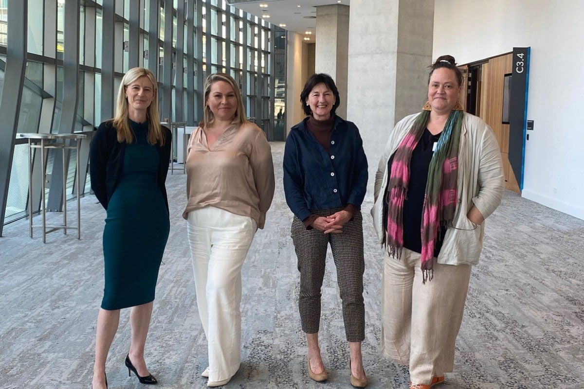 Four smiling women looking towards the camera whilst standing inside the lobby of a large building