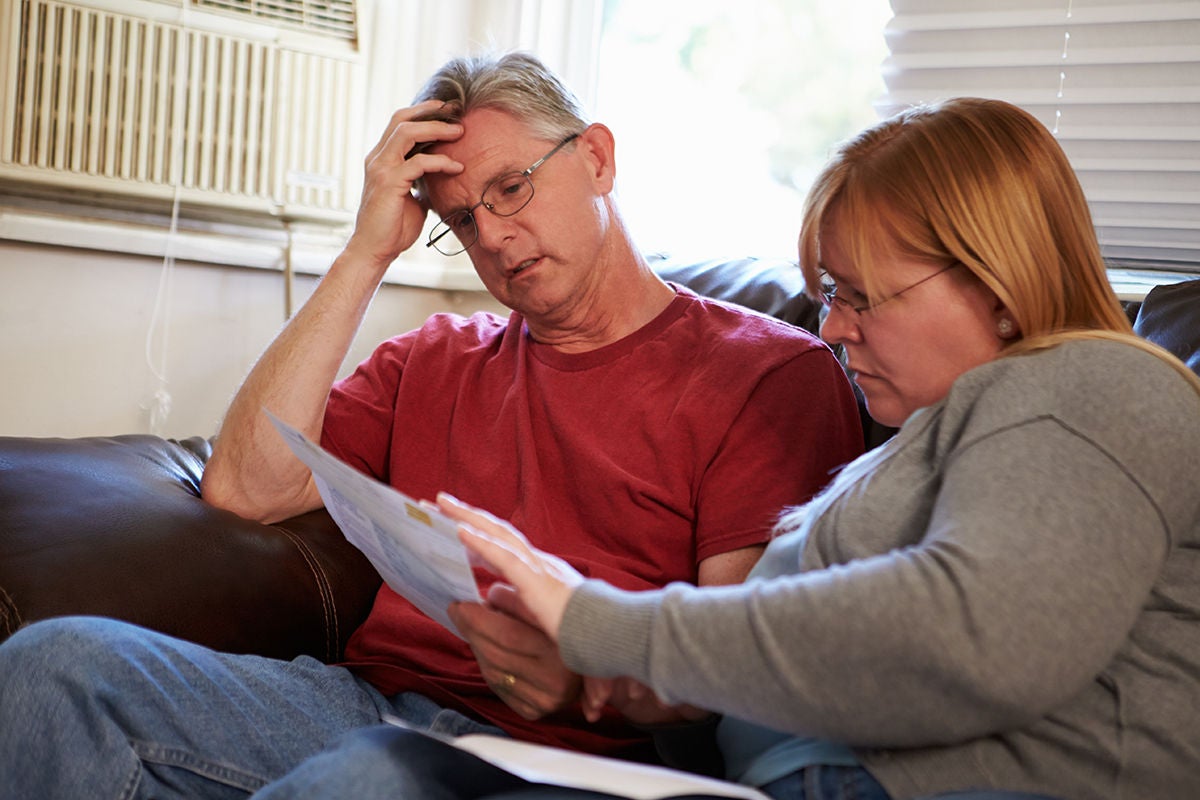 Worried Couple Sitting On Sofa Looking At Bills