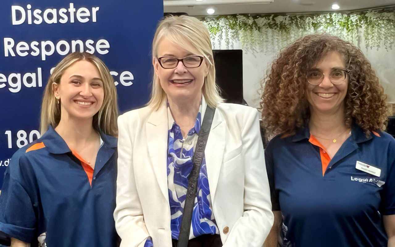 Photo of three people standing together smiling, with part of a Disaster Response Legal Service banner behind them. To the left is Disaster Response Legal Service solicitor, Natalie Bechara. In the middle is Joanna Quilty, Head of Preparedness and Recovery at NSW Reconstruction Authority. To the right is Disaster Response Legal Service solicitor, Ayala Amber.
