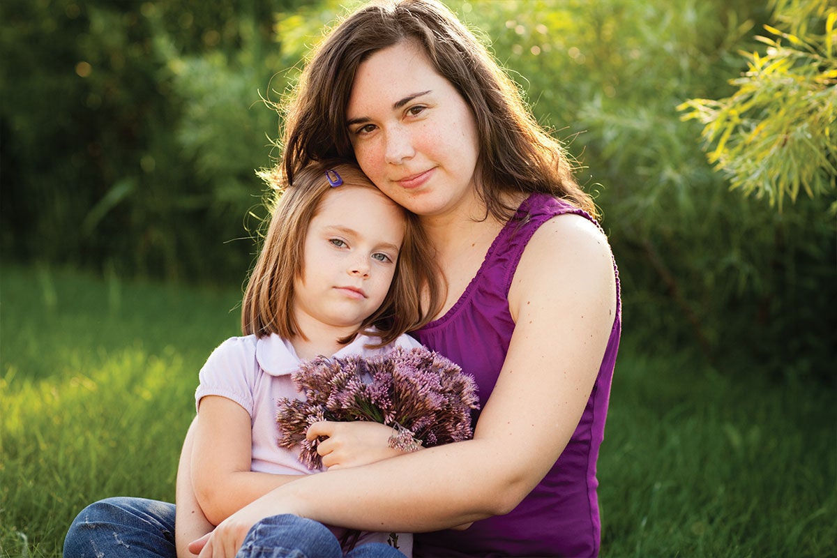 Mum with daughter sitting on her lap looking at camera with a partial smile