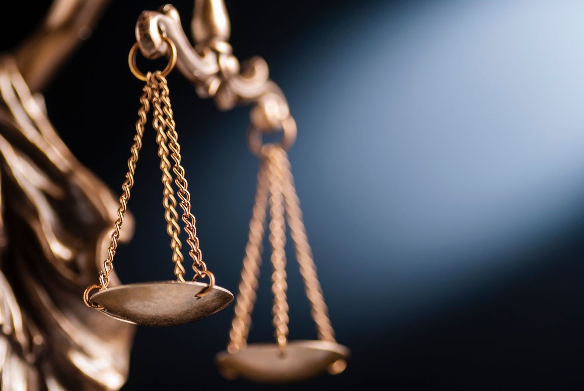 Close up on the scales of justice on a small bronze statue over a blue background with copy space conceptual of law and order