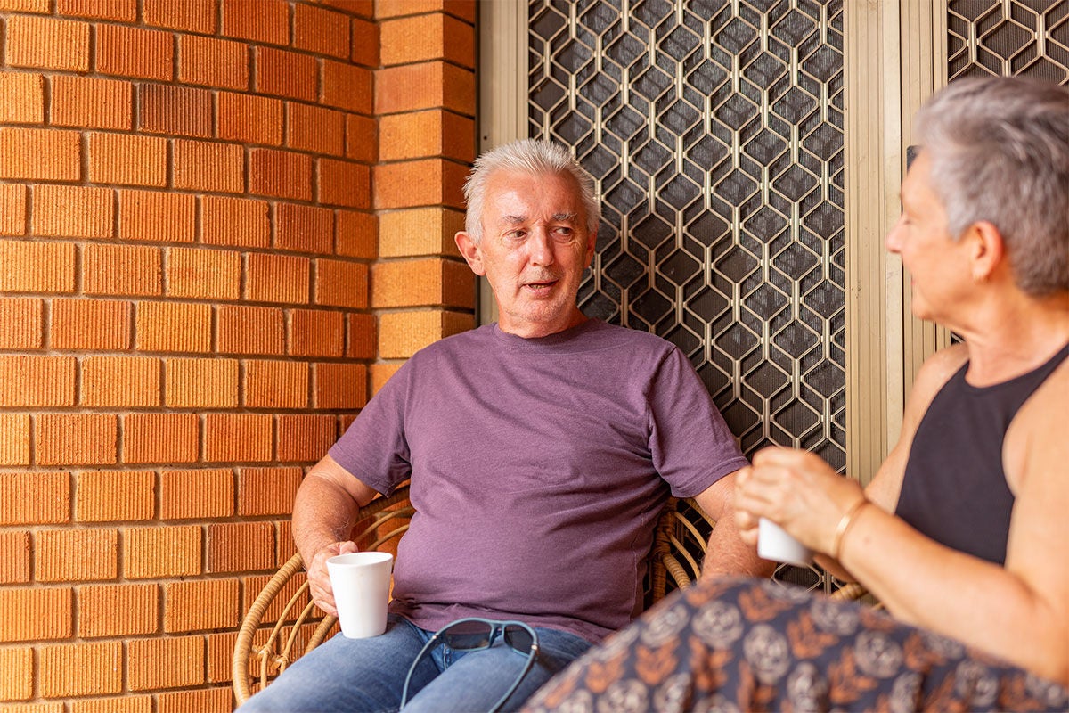Older man and lady sitting at the front of the house having coffee and in covnersation