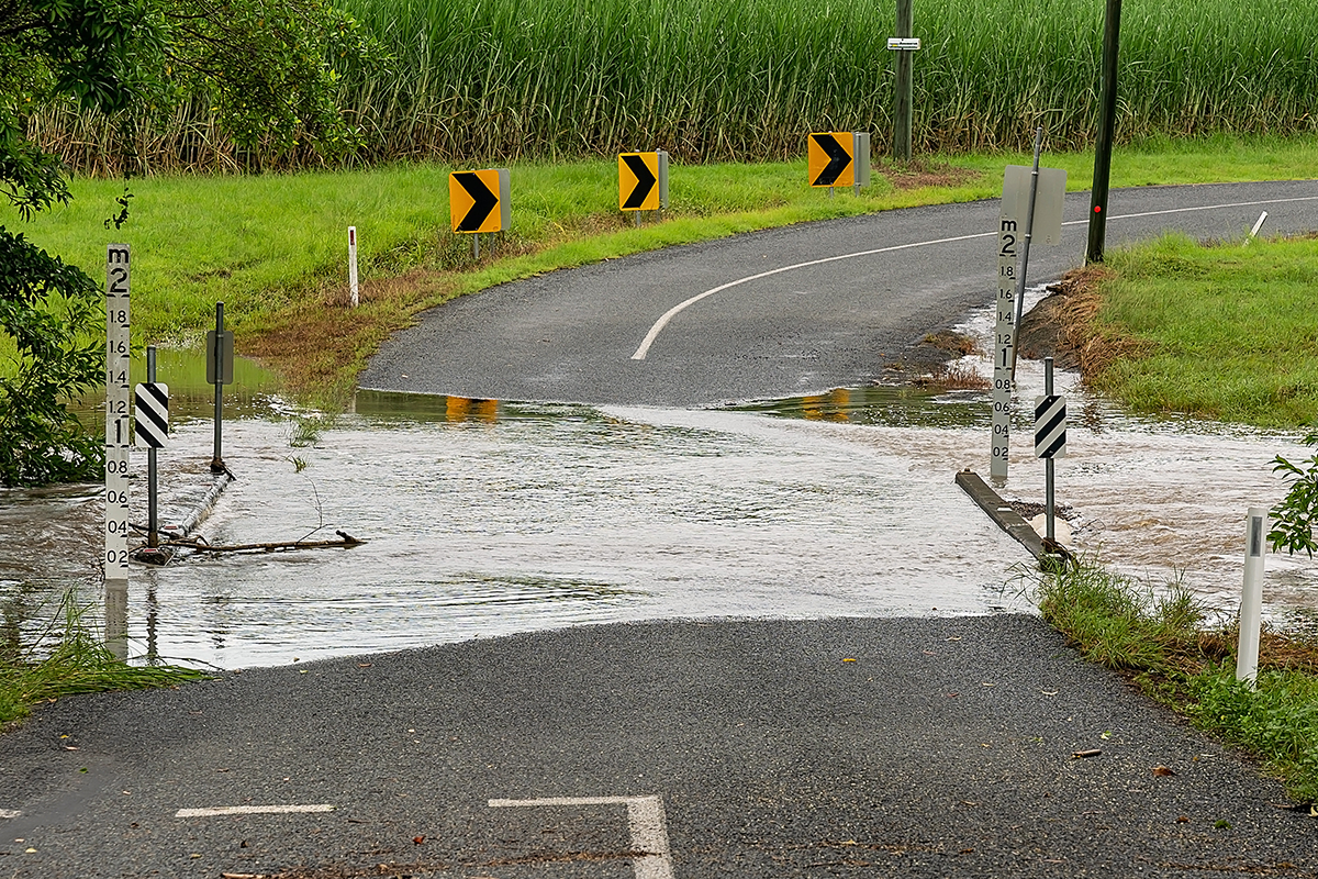 A road somewhere in regional Australia is blocked by a flooded creek. Signs measure the water level at just under 0.2m.