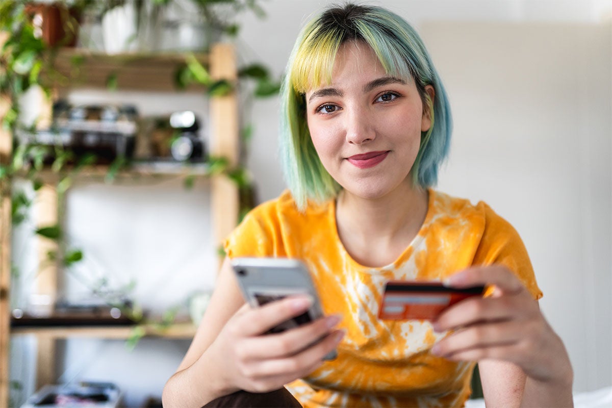 Lady with blue and yellow hair in a bob holding a phone and credit card