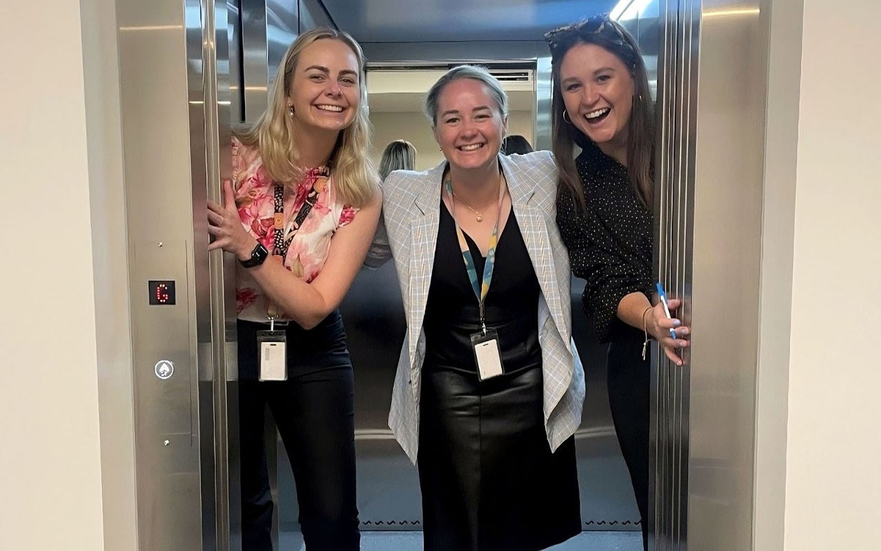 Photo of three people standing together inside elevator doors, smiling. To the left is Geraldyne Keen, in the middle is Megan Raines and to the right is Hannah Higgins, who are Dubbo-based family lawyers.