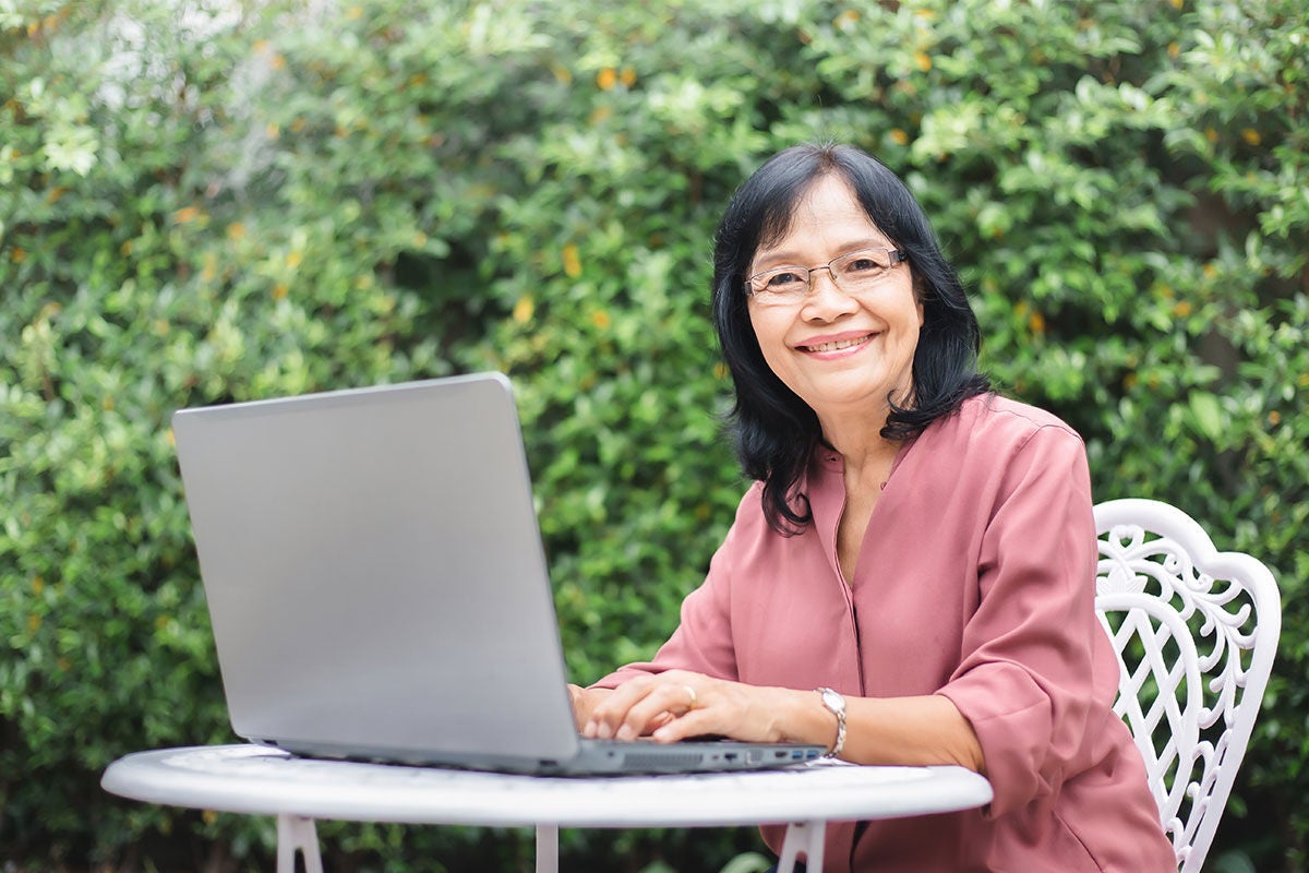 Middle aged lady sitting in garden in front a of a computer looking at the camera smiling