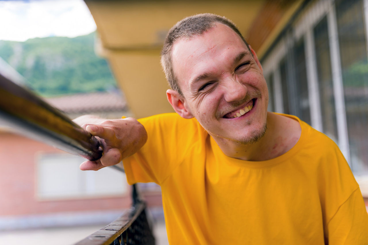 Portrait of a man with disability, wearing a bright yellow t-shirt and smiling directly at the camera.